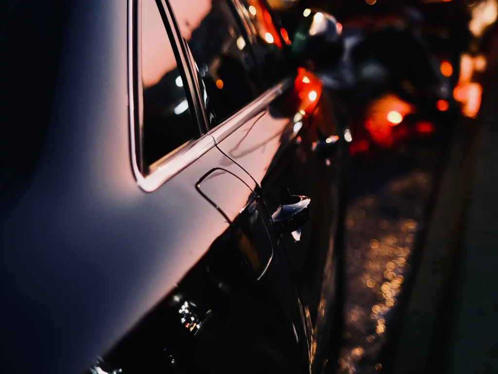 Close-up of a black car door reflecting warm city lights at dusk